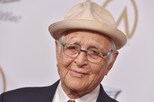 Norman Lear wearing a black suit and a beige hat.