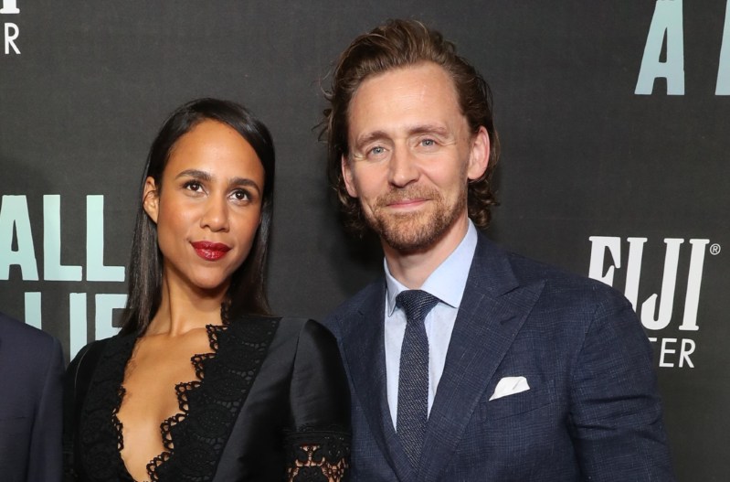 Tom Hiddleston in a navy blue suit standing with Zawe Ahston who is wearing a black dress.