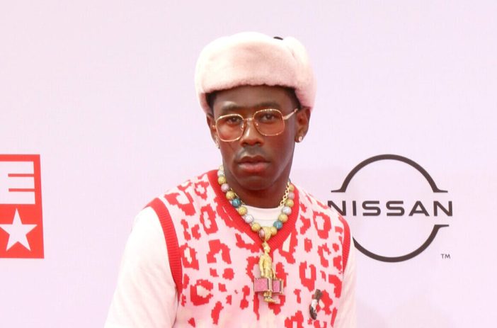 Tyler The Creator at the 2021 BET Awards wearing a wearing white, fuzzy hat, glasses, and red and white leopard print sweater vest