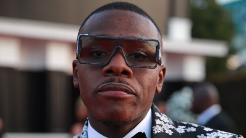 DaBaby peers at the camera from behind sunglasses while wearing a floral patterned suit