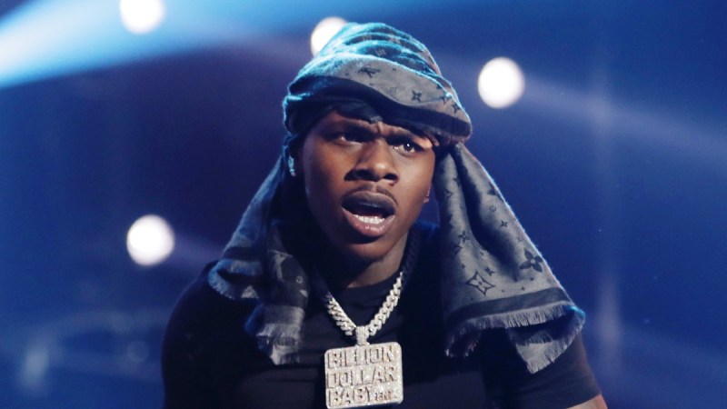 DaBaby performs onstage wearing a black shirt and gray scarf on his head