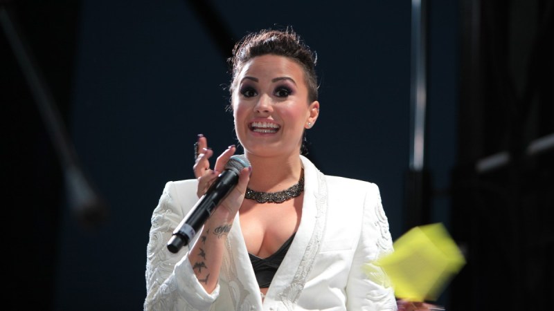 Demi Lovato wears a white suit jacket and holds a microphone