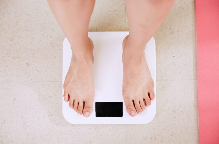 Image of woman weighing herself on a scale.