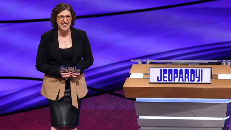 Mayim Bialik laughs on the set of Jeopardy beside an empty podium