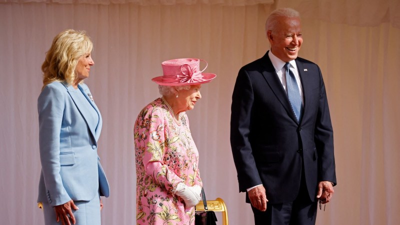 Dr. Jill Biden, Queen Elizabeth, and President Joe Biden stand together on a platform