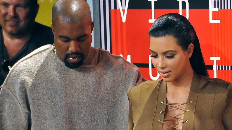 Kanye West wears a gray sweat suit and stands with Kim Kardashian, in an olive dress, at the VMAs