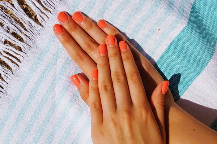 Image of orange painted nail on top of a beach blanket.