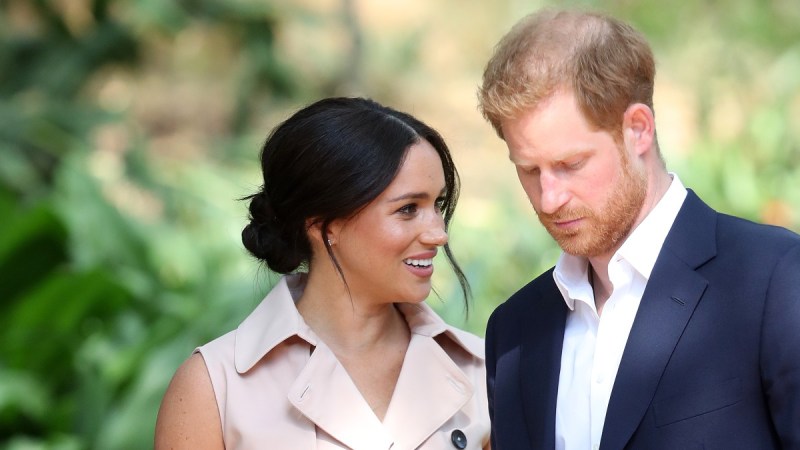 Meghan Markle, in a beige dress, smiles at Prince Harry, in a dark suit, while outside