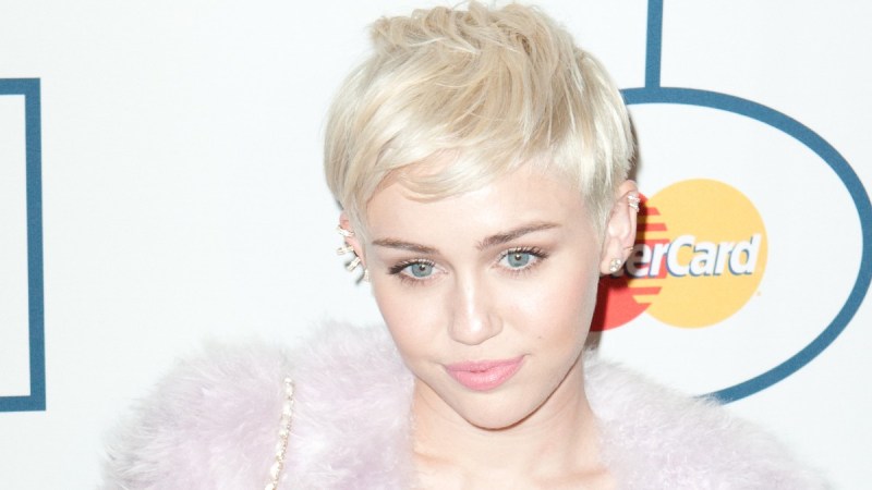 Miley Cyrus wears a feathery pink coat over a short white dress on the red carpet