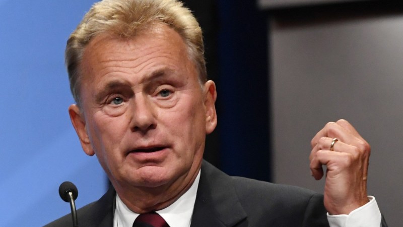 Pat Sajak stands onstage behind a podium wearing a dark suit as he gives a speech