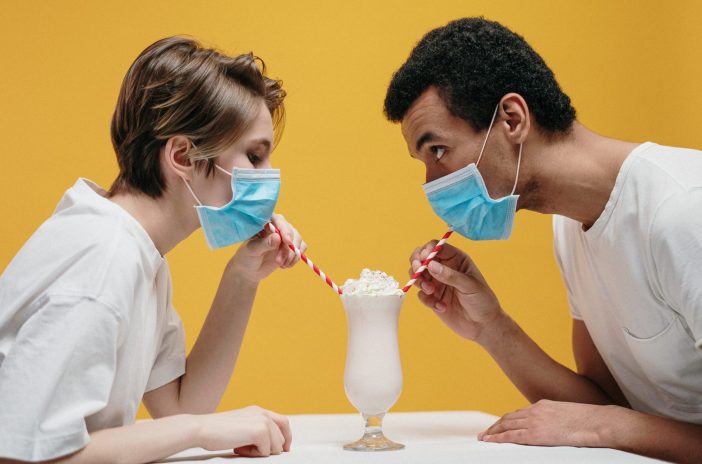 Man and woman sharing a milkshake while wearing masks.