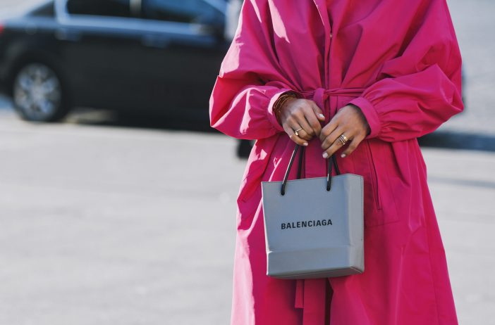 Image of woman wearing a pink dress holding a Balenciaga bag in the city.