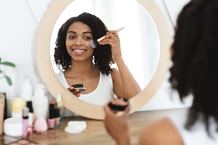 Image of woman applying blush in the mirror.