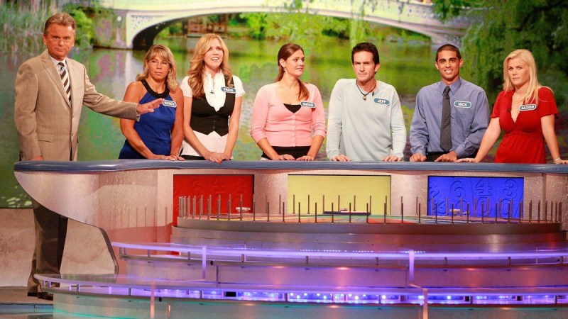 Pat Sajak stands with six celebrity contestants on the set of Wheel Of Fortune