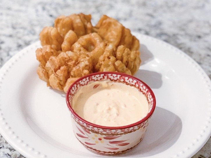 Copycat Texas Roadhouse Blooming Onion on serving plate with bowl of dipping sauce.