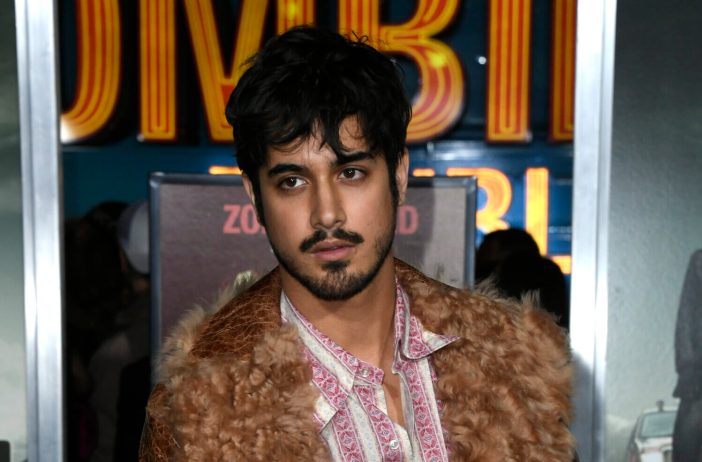 Avan Jogia wearing a brown vintage jacket and pink and white striped button down at the Zombieland 2: Double Tap premiere in 2019