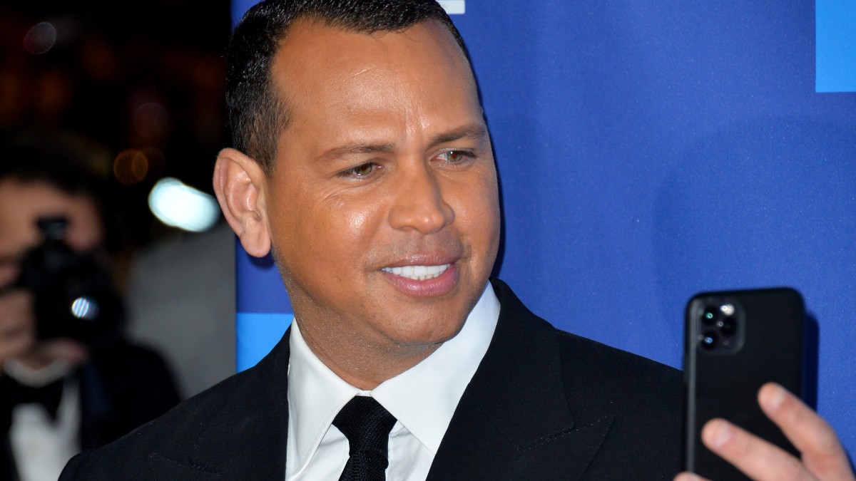 Alex Rodriguez holds up his phone to take a photo of an out of frame Jennifer Lopez on the red carpet