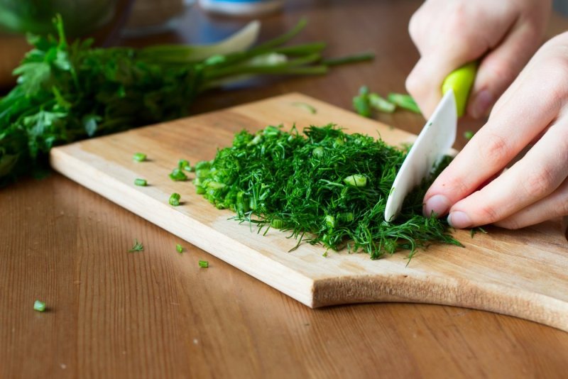 Cutting fresh herbs with a ceramic knife on wooden board. Cooking