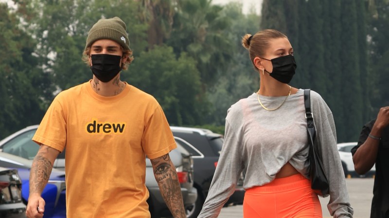 Justin Bieber wears a yellow shirt and strolls hand in hand with wife Hailey, in a gray shirt and orange shorts