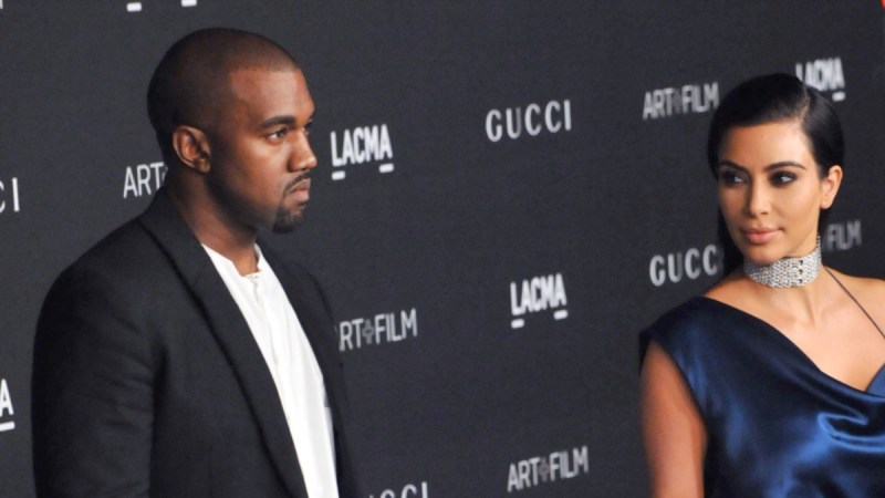 Kanye West wears a dark suit and stands slightly apart from estranged wife Kim Kardashian, in a blue dress