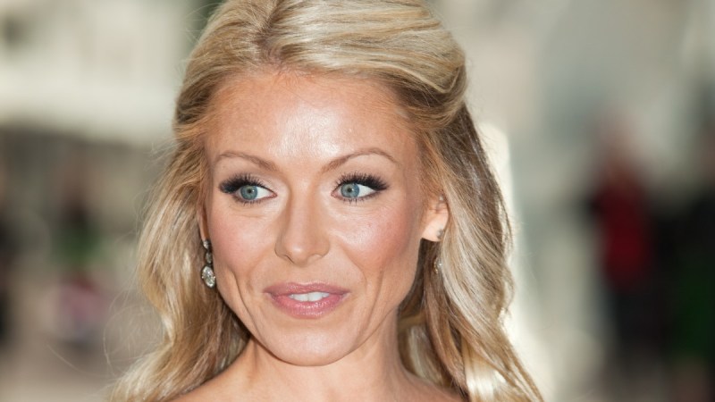 Kelly Ripa wears a strapless blue gown against a blurry background