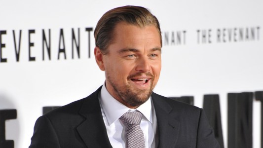 Leonardo DiCaprio laughs while wearing a dark suit on the red carpet