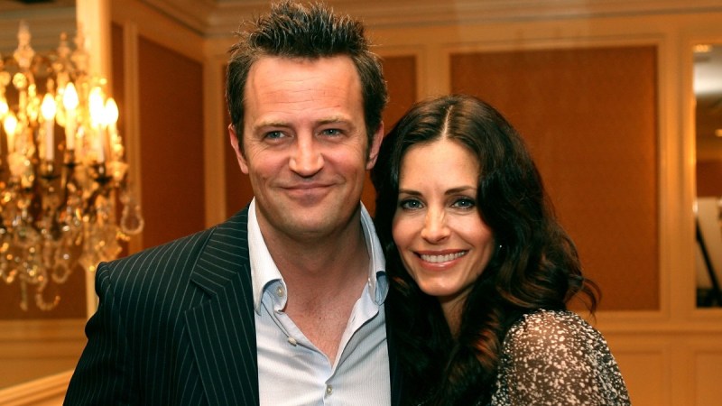 Matthew Perry wears a dark suit jacket as he poses beside Courteney Cox in a speckled green gown