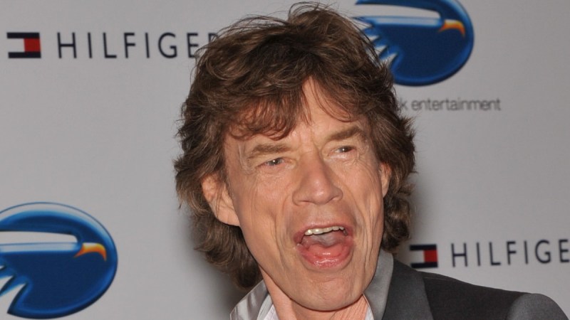 Mick Jagger wears a gray suit and pulls a face at photographers while walking the red carpet