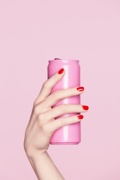 Nails Design. Red Manicure On Woman Hands. Close Up Of Female Hand With Soft Skin And Red Nail Polish Holding Pink Soda Can On Pink Background. High Resolution.