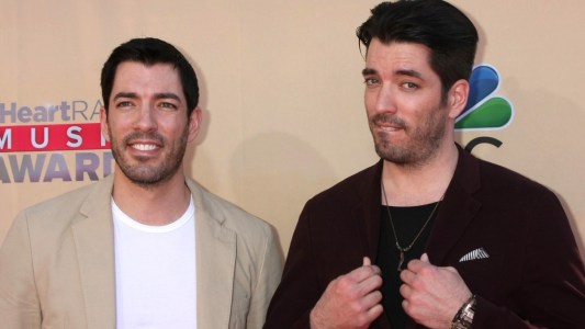 Johnathan and Drew Scott pose together on the red carpet against a pale tan background