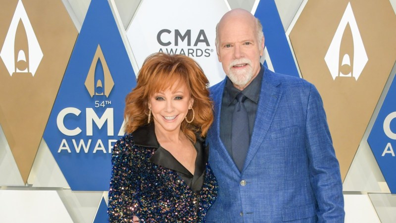 Reba McEntire wears a black dress and poses with Rex Linn, in a blue suit, on the CMA red carpet