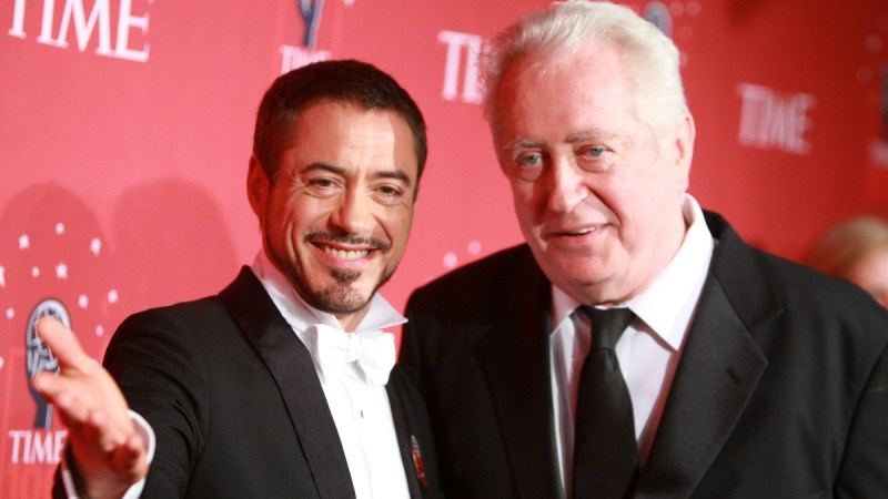 Robert Downey Jr, in a tux, stands with father Robert Downey Sr, in a black suit, on the red carpet