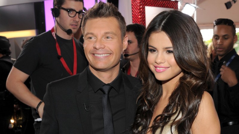 Ryan Seacrest, in a black suit, and Selena Gomez, in a gold dress, pose together at the Grammy's