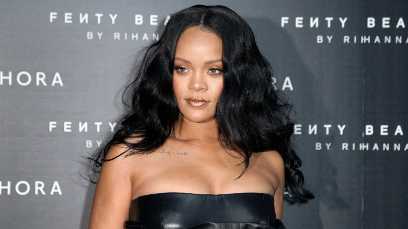 Rihanna wears a black dress in front of a grey background