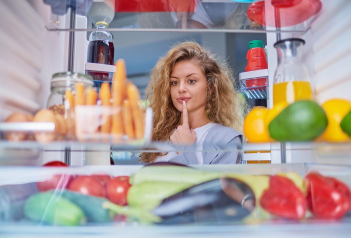 A woman looking undecided while looking inside a fridge full of food.