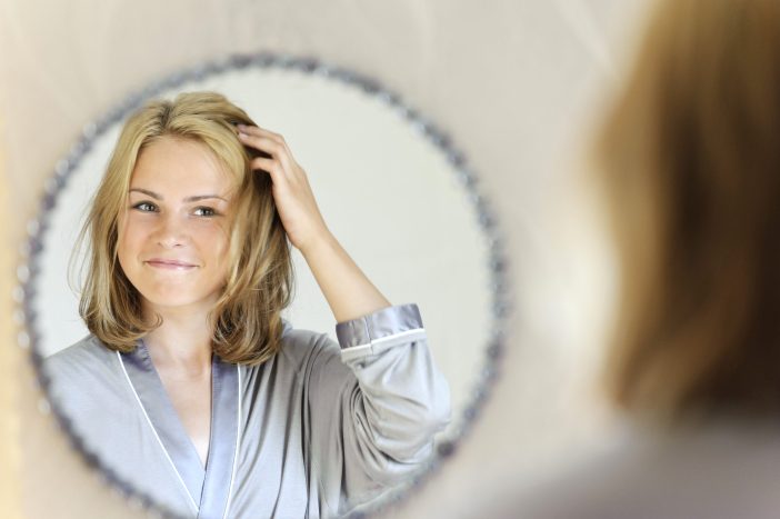 Woman touching her hair in the mirror.
