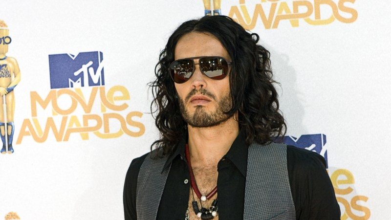 (Dooley Productions/Shutterstock.com) Russell Brand wearing a vest and sunglasses