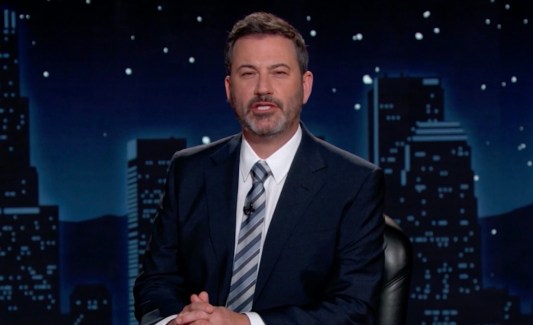 Jimmy Kimmel in a suit sitting at a desk