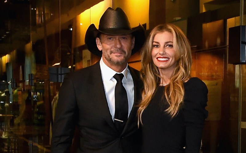 Tim McGraw smiling in a suit and cowboy hat with Faith Hill in a black dress