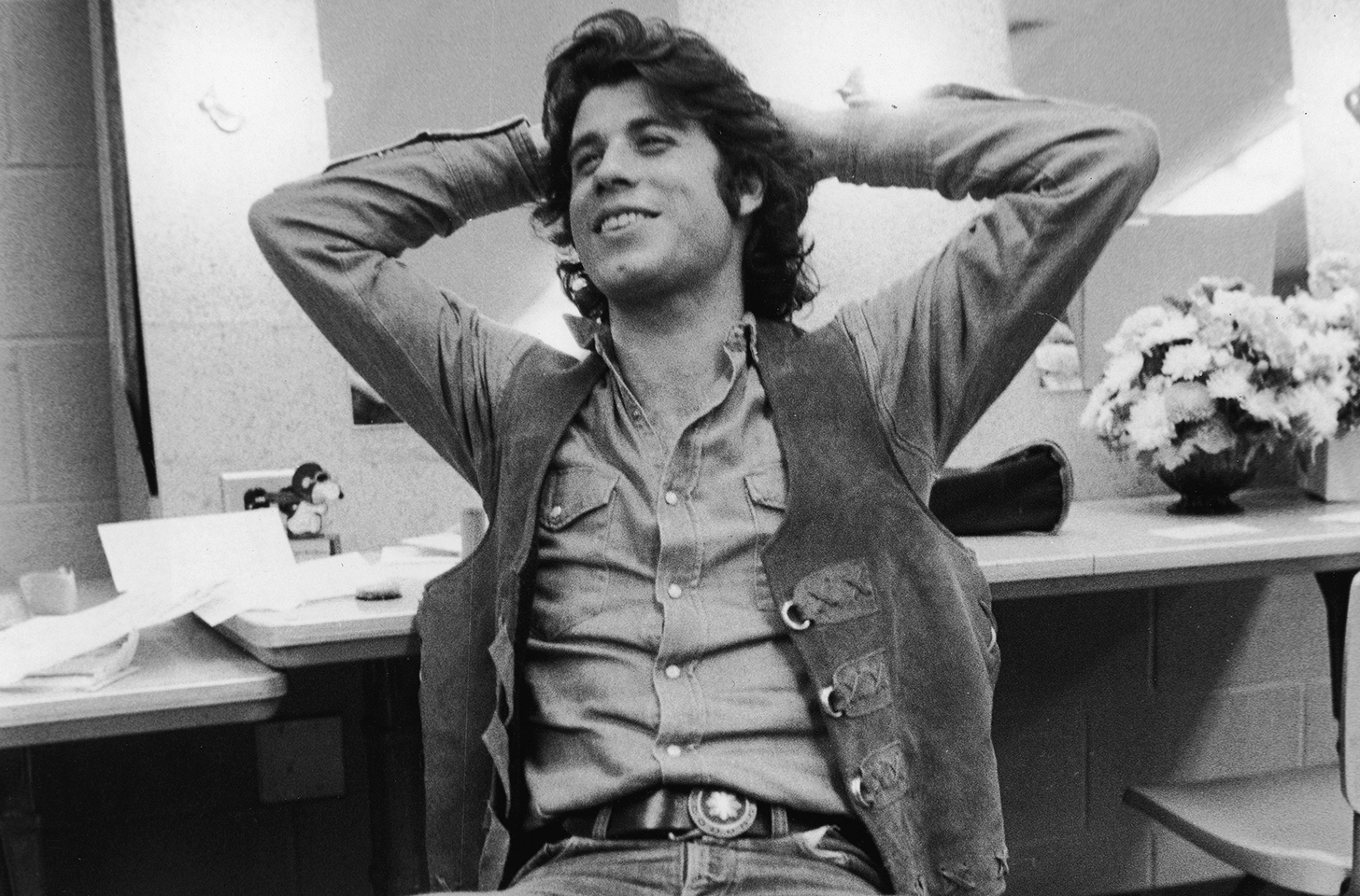 Black and White photo of John Travolta in the late 1970s with his hands behind his head.