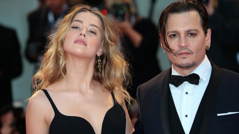 Amber Heard wears a black dress and tosses her hair as she stands next to Johnny Depp, in a black tux, on the red carpet