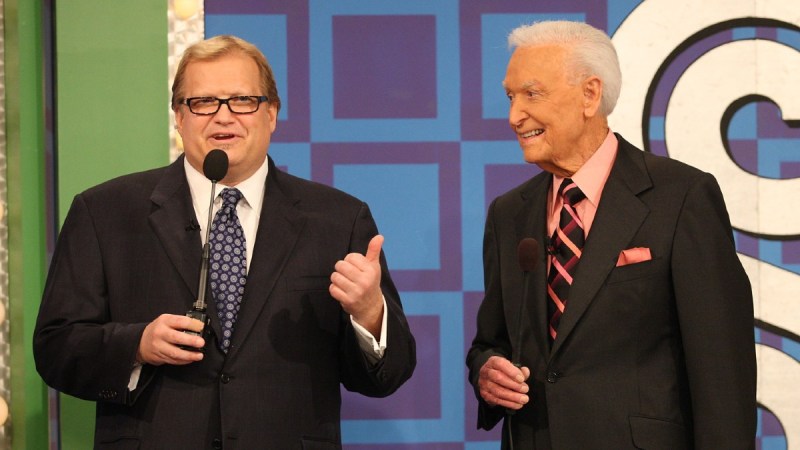 Drew Carey and Bob Barker, both wearing dark suits, stand together on the set of Price Is Right