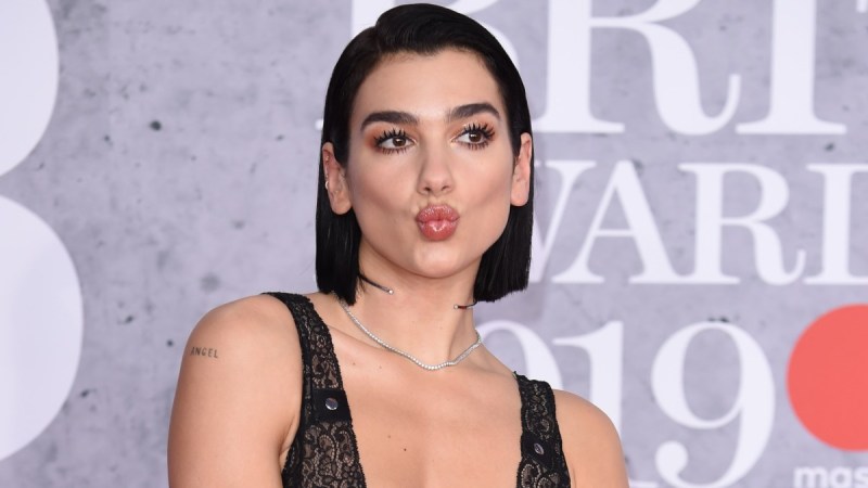 Dua Lipa pulls a kissy face while wearing a black and pink dress on the red carpet