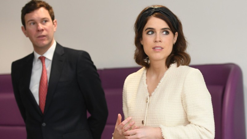 Jack Brooksbank wears a black suit and stands slightly behind his wife, Princess Eugenie, in a cream blouse