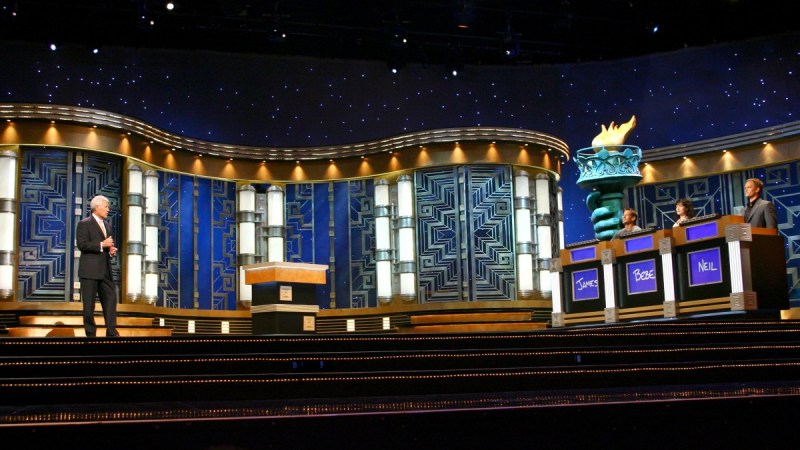 Host Alex Trebek faces three contestants on the stage of Jeopardy!