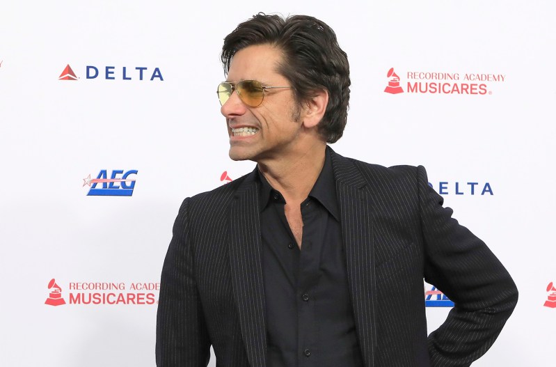 Jphn Stamos in sunglasses, looking to the right and grimacing.