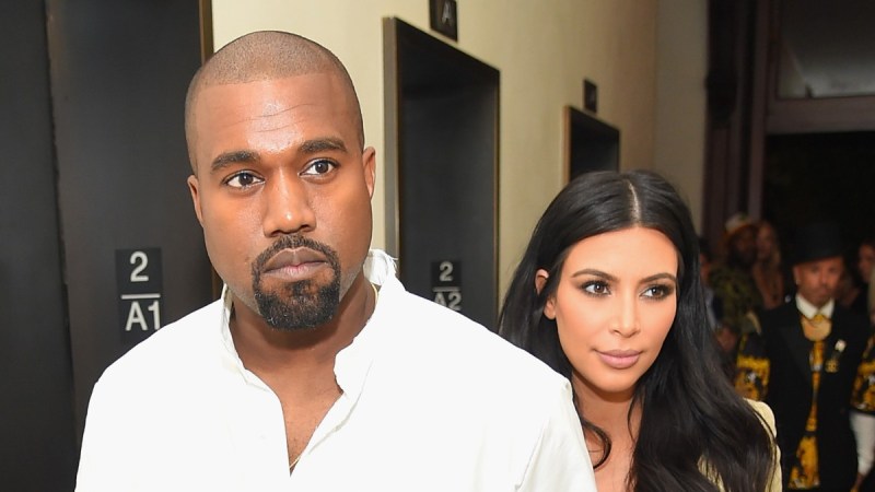 Kanye West, wearing a white shirt, and Kim Kardashian, in brown, walk through a hallway