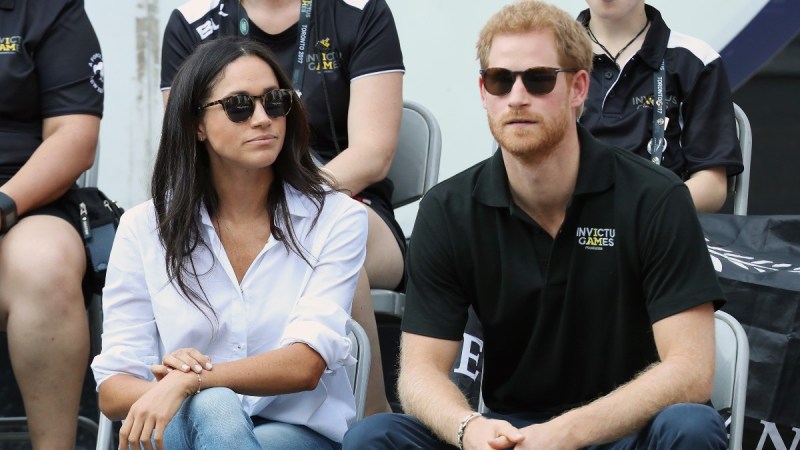 Meghan Markle, in a white top, sunglasses, and jeans, sits with Prince Harry, in a black top, sunglasses and jeans, at the Invictus Games