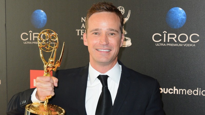 Mike Richards holds up an Emmy while wearing a black suit on the red carpet