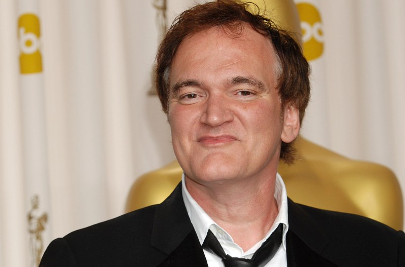 Quentin Tarantino smiling smugly in a suit.